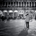 Anima Mia — Couple in Piazza San Marco, woman holding onto her companion as they listen to the orchestra, lost in their own world — Venice — Alessandro Cancian